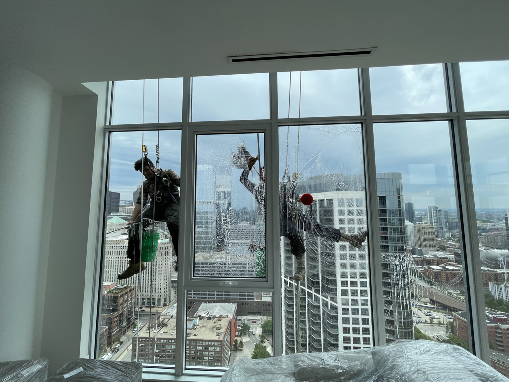 Two Green Clean Window Wash employees working on the high-rise apartment window cleaning with a squeegee