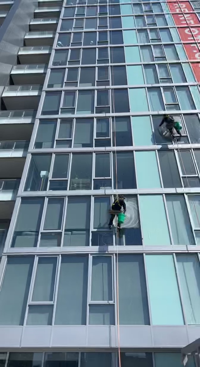 2 window washers cleaning exterior windows of a high rise luxury apartment building
